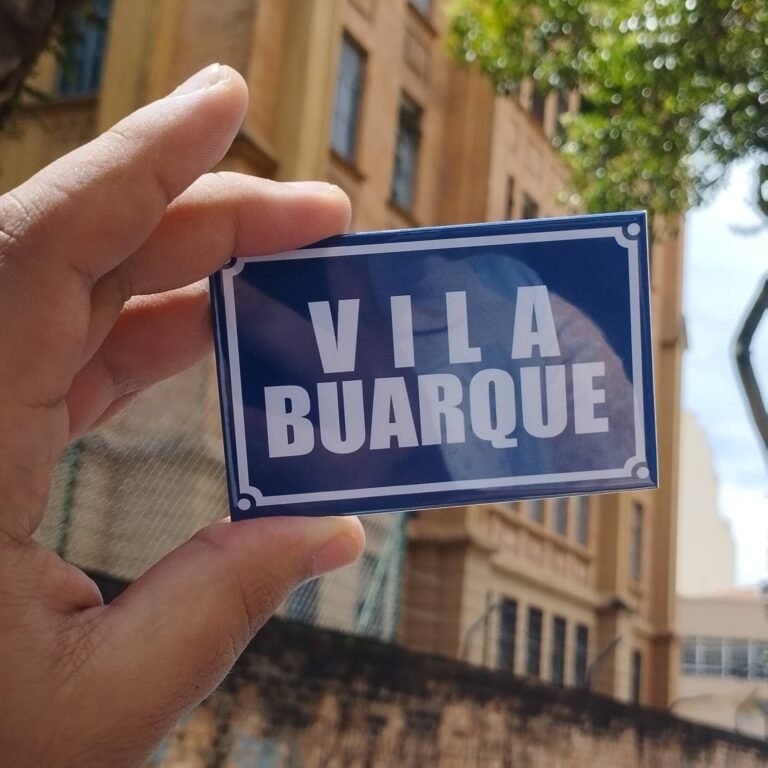 Imagem de uma miniatura de placa do bairro Vila Buarque, com a Santa Casa de São Paulo ao fundo. 2023.