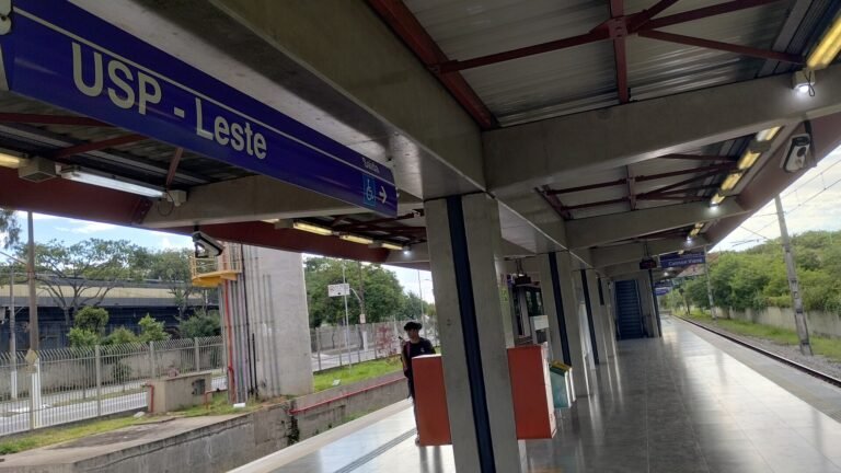 Placa com o nome da estação USP-Leste da Linha 12-Safira da CPTM, indicando também o sentido da saída. Ao fundo desta im