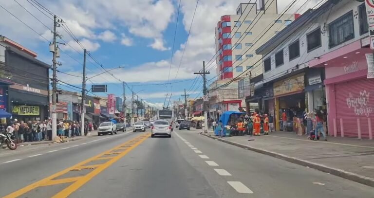 Vista da Avenida Mateo Bei, região comercial de São Mateus, com movimento de veículos, ônibus, pedestres e estabelecimen